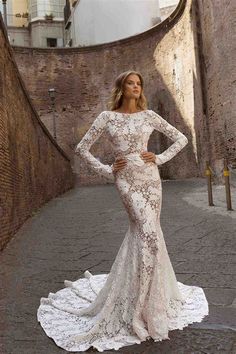 a woman in a long sleeved wedding dress standing on the street with her hands on her hips