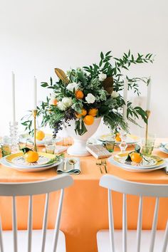 the table is set with oranges, white flowers and greenery for an elegant dinner