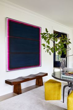 a dining room table with two yellow chairs and a large painting on the wall behind it