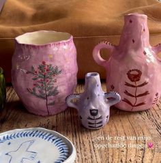 three ceramic vases sitting on top of a wooden table next to a bowl and plate