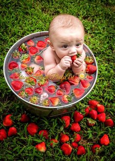 a baby sitting in a metal bowl with strawberries on the ground next to it