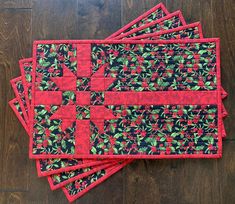 four placemats with red and green designs on them sitting on a wooden floor