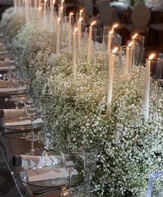 a long table with candles and flowers in vases on top of each other, along with place settings for the tables