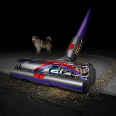 a dog standing next to a vacuum cleaner on the ground in the dark with it's head up