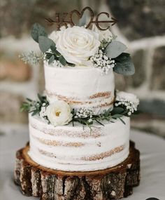 a wedding cake with white flowers and greenery is on top of a tree stump