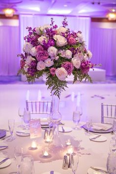 a vase filled with purple and white flowers on top of a table covered in silverware