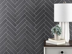 a lamp on top of a dresser next to a wall with grey herringbone tiles