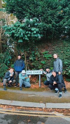 some people are sitting on the side of a road and posing for a photo in front of a sign