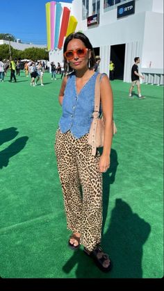 a woman standing on top of a green field wearing leopard print pants and red sunglasses