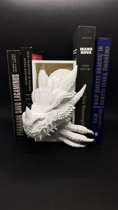 a white dragon statue sitting next to books on a black surface with the bookcase behind it