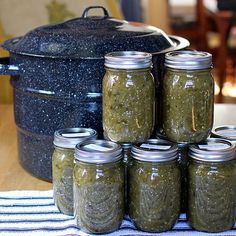 six jars of pickles sit in front of an open slow cooker on a table