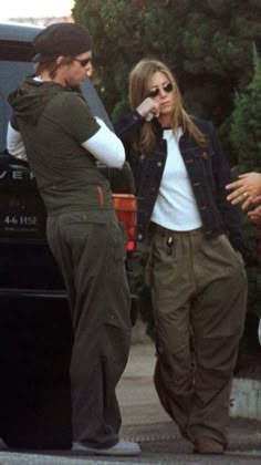 two men and a woman standing in front of a car talking on their cell phones