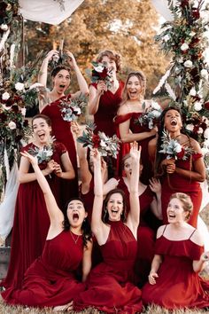 a group of women in red dresses standing next to each other with their hands up