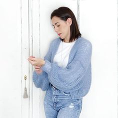 a woman standing in front of a white door looking at her cell phone while wearing ripped jeans and a blue cardigan