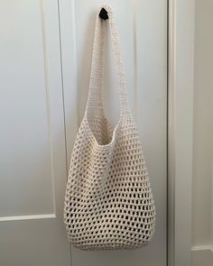 a crocheted bag hanging on a door with the handle down and it is white