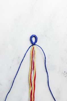 a piece of colorful string hanging from a hook on a white surface with blue and red thread