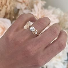 a person's hand with a ring on it and some flowers in the background