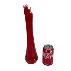 a coca cola can next to a red glass vase with a silver top and bottom