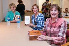 three women are sitting at a table with water bottles and books in front of them