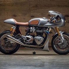 a silver and brown motorcycle parked in front of a wooden wall with no one on it