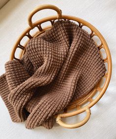 a brown knitted hat sitting on top of a wooden basket next to a white blanket