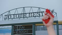 a person holding up a red object in front of a stadium sign that reads do your best