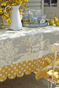 a table with yellow flowers on it and a white vase filled with lemons next to the table