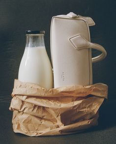 a bottle of milk next to a white purse on top of a brown paper bag