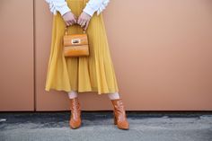 Orange Gaia croc-embossed handbag. Model wearing yellow skirt, white top. Bamboo handle, clasp with gold hardware. Harrods, Gold Hardware