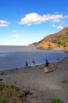 three people are standing on the beach by the water