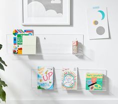 three clear acrylic shelves holding greeting cards and magnets on the wall next to a potted plant