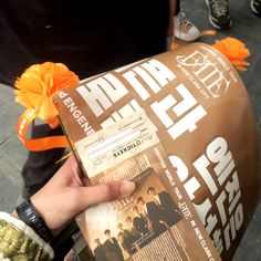 a person holding up a movie ticket in front of their face with an orange flower