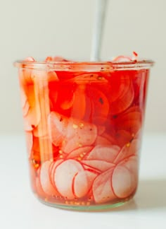 a jar filled with pickled onions on top of a white table next to a spoon