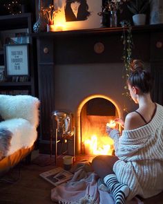 a woman sitting on the floor in front of a fire place holding a lit candle