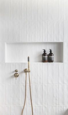 a white tiled shower with brass fixtures and soap dispensers on the wall