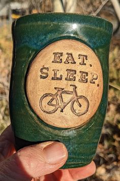 a hand holding up a green cup with a bike on it that says eat sleep