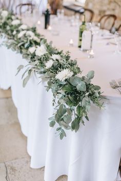 the table is set with white flowers and greenery