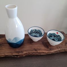 three bowls and a vase sitting on a wooden tray with a mountain scene painted on it