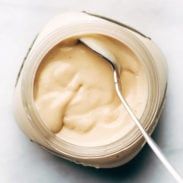 a spoon in a jar filled with mayonnaise on top of a white table