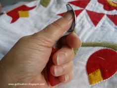 a hand holding a metal object in front of a quilt