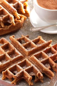 two waffles on a plate next to a cup of coffee and some sugar