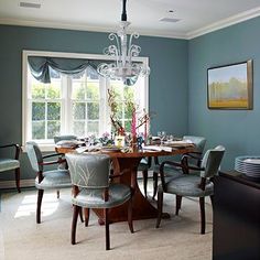 a dinning room with blue walls and white trim on the ceiling, chairs around a wooden dining table