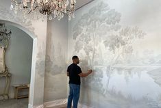 a man standing in front of a wall with a painting on it and a chandelier hanging from the ceiling