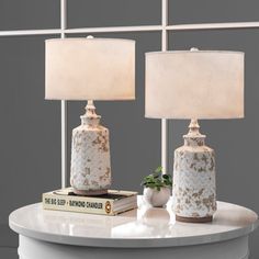 two white vases sitting on top of a table next to a book and lamp