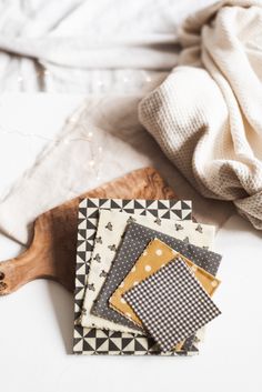 four pieces of fabric sitting on top of a wooden cutting board next to a white blanket