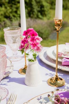 pink flowers are in a white vase on a table set with plates and silverware