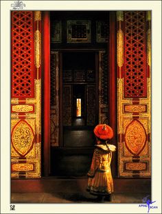 a woman standing in front of a doorway with an orange hat on her head and wearing a yellow dress