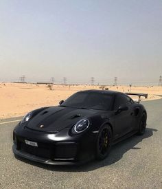 a black sports car parked on the side of a road in front of sand dunes