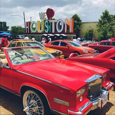 an old red car is parked in front of the houston sign and other classic cars