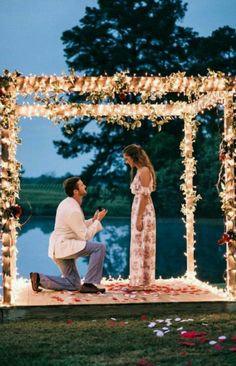 a man kneeling down next to a woman in front of a lit up gazebo